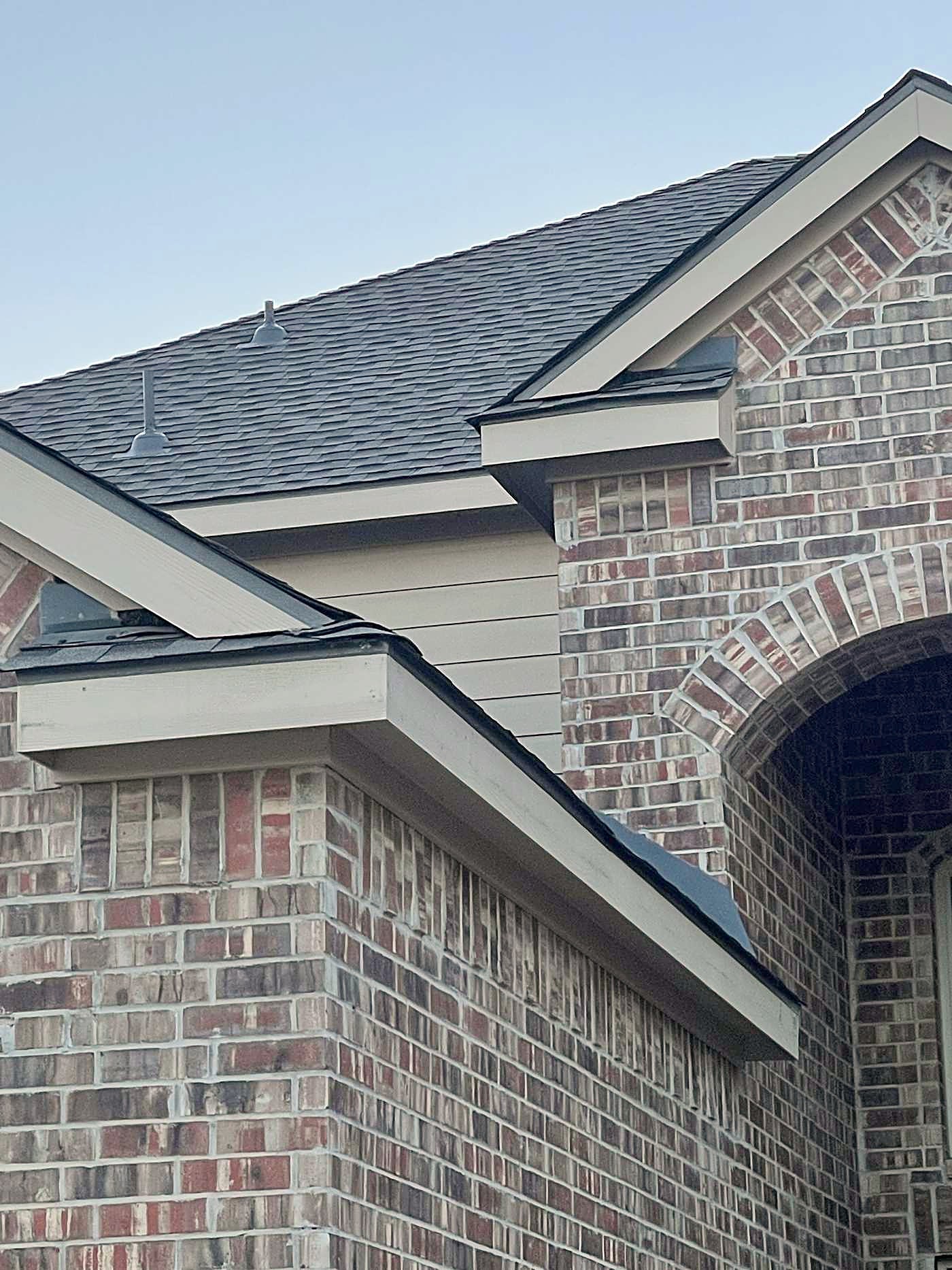 Close view of a brick gable and arched entry under a gray shingle roofline