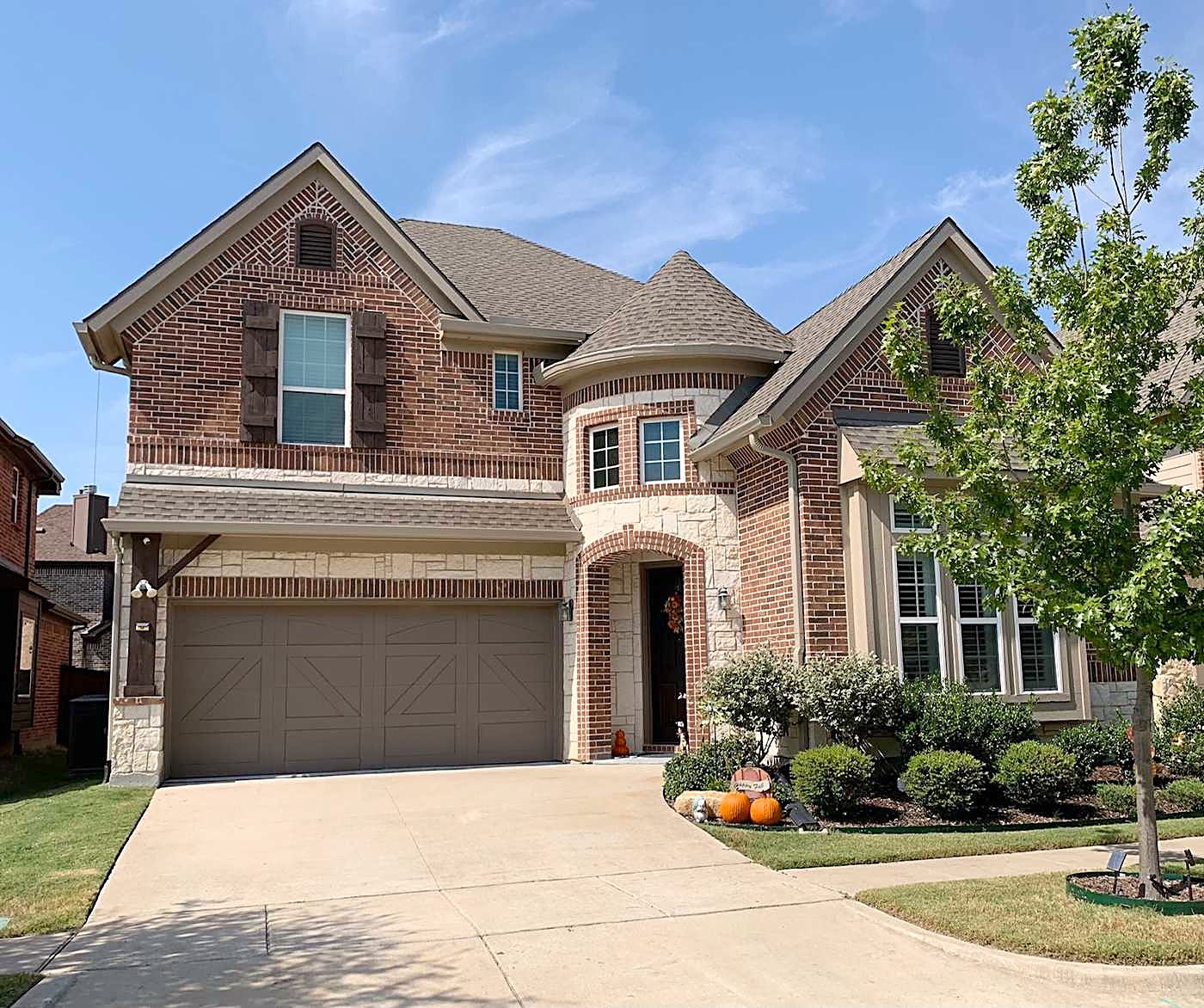 Brick two-story home with a gray shingle roof, a covered entry and a double driveway