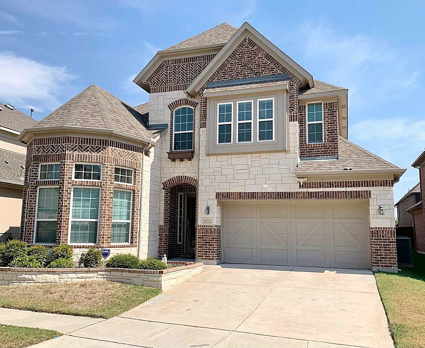 Two-story brick and stone home with a turret, a gray shingle roof and a front-facing garage