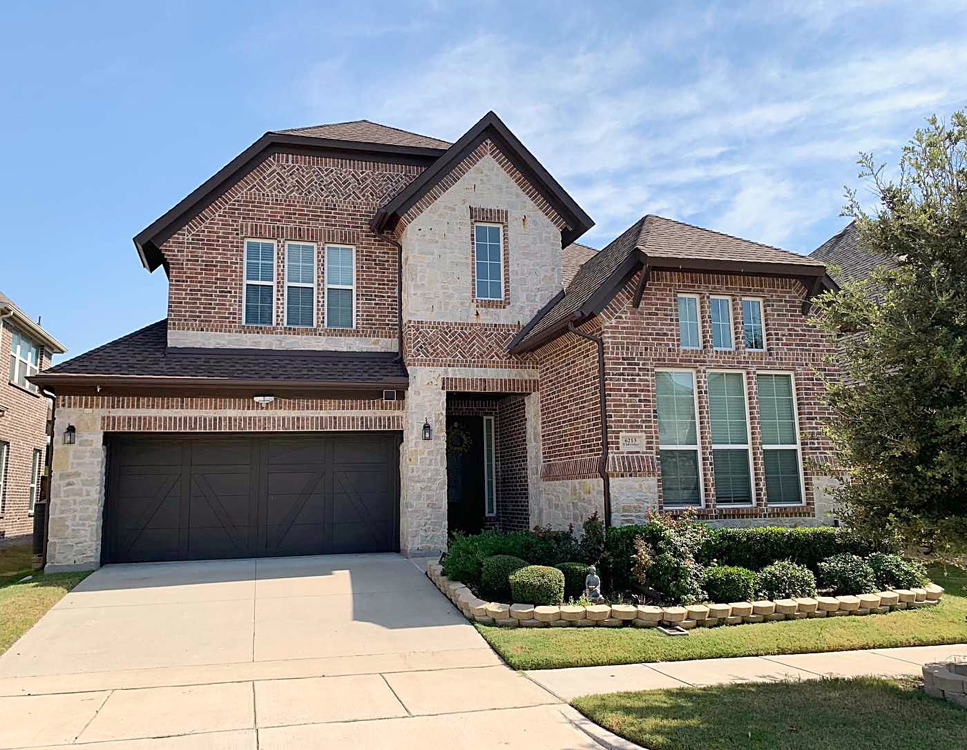 Brick and stone two-story home with a dark shingle roof and a wide garage door