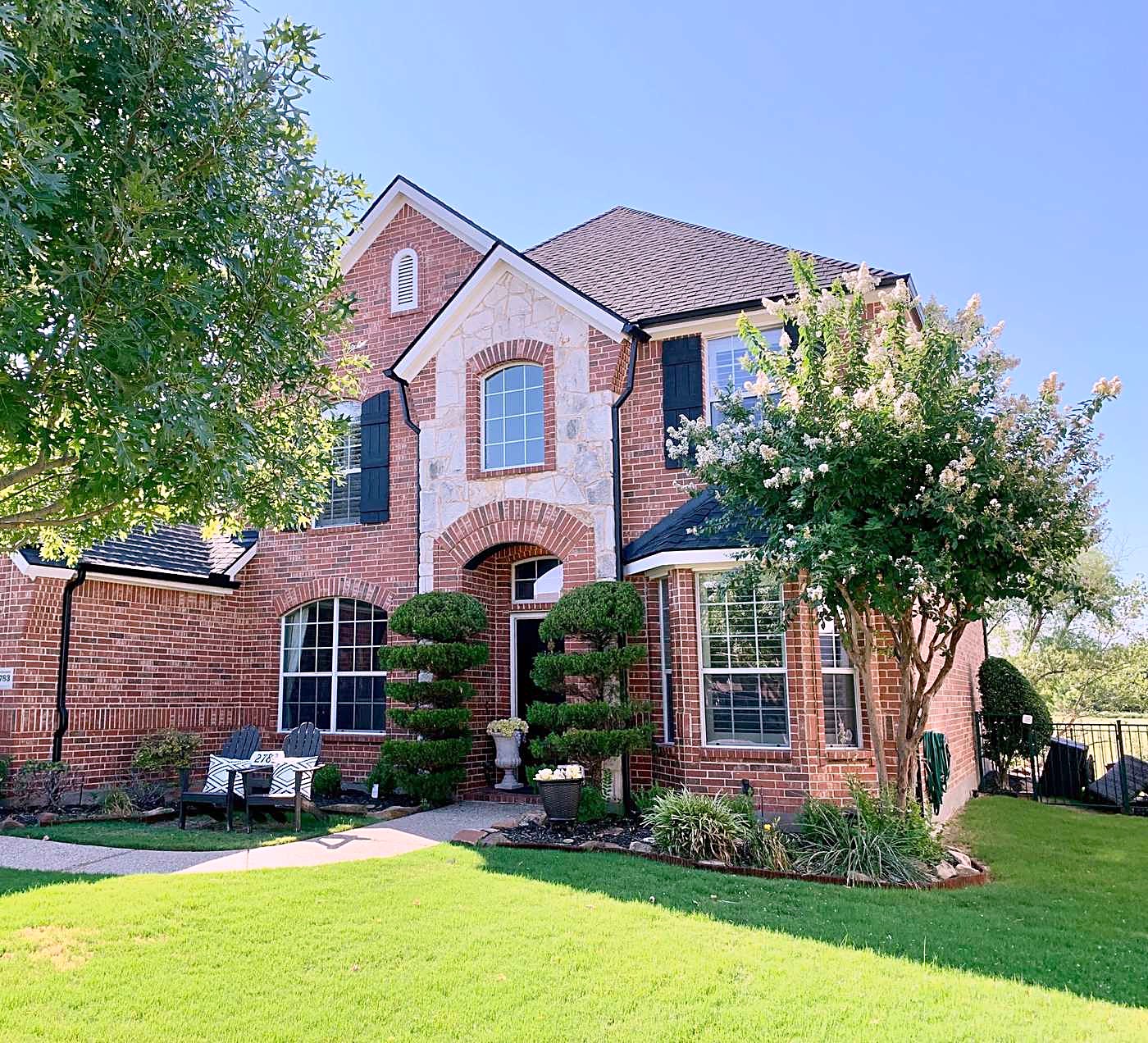 Red brick two-story home with stone trim, black shutters and a flowering crape myrtle in front