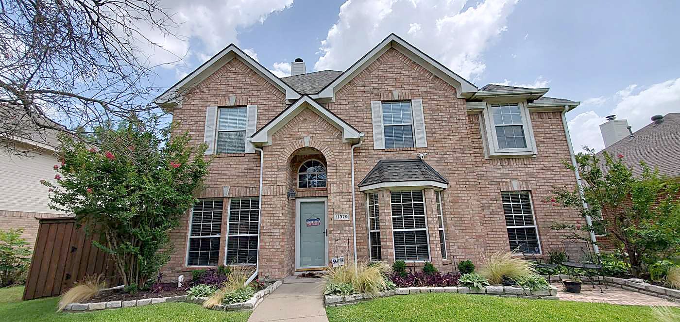 Two-story brick home with a gray shingle roof, arched front windows and a wood fence at the side