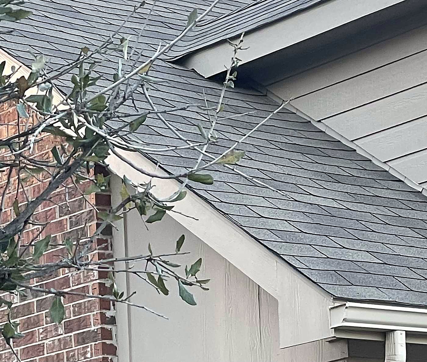 Gray shingle roof edge meeting a light siding wall beside a brick column