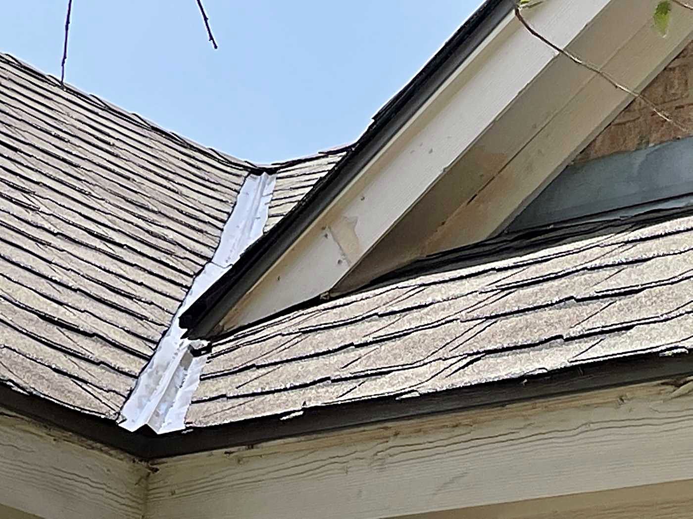 Close view of weathered shingles where a roof valley meets a gable, with the metal flashing lifted