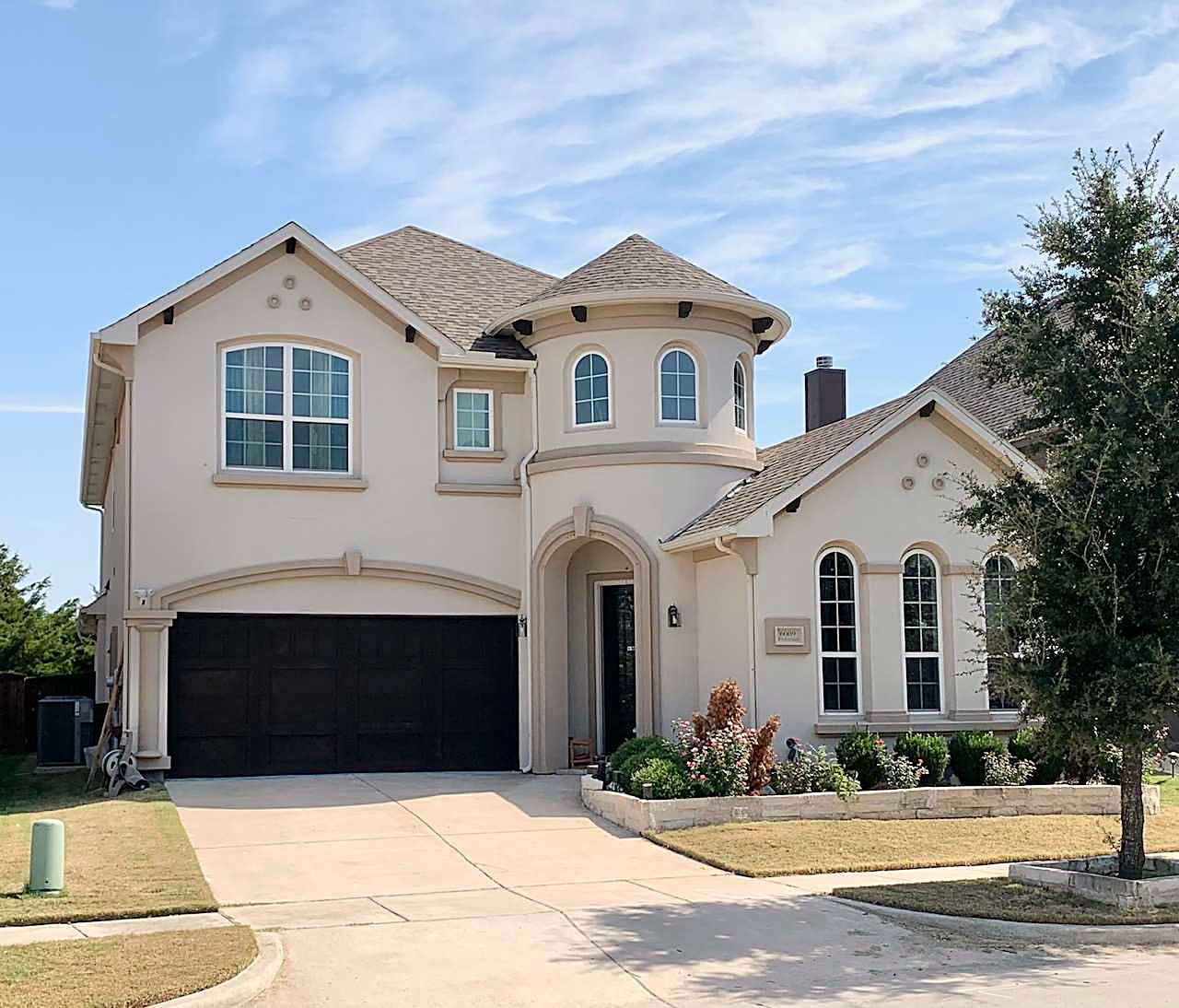 Cream stucco home with a round turret, a brown shingle roof and a dark garage door