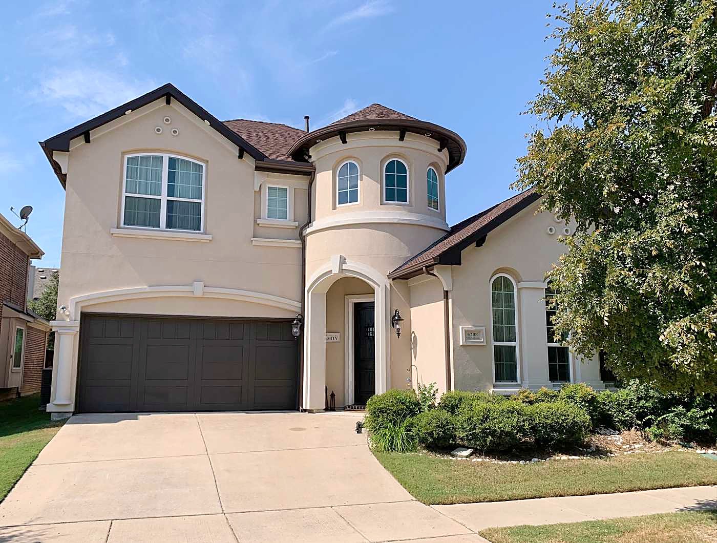Two-story stucco home with a round tower, a brown roof and a landscaped front bed