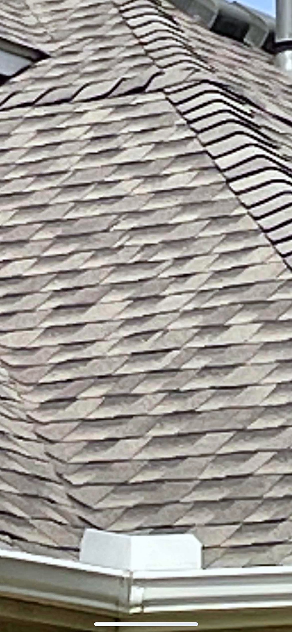 Close view of a weathered tan shingle slope running down to a white gutter