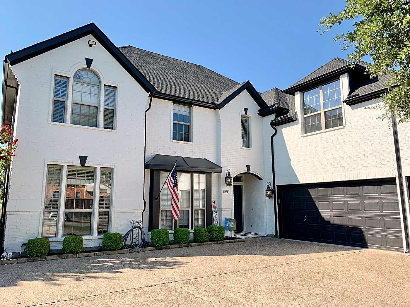 Painted white brick home with a charcoal shingle roof, black gutters and a dark garage door
