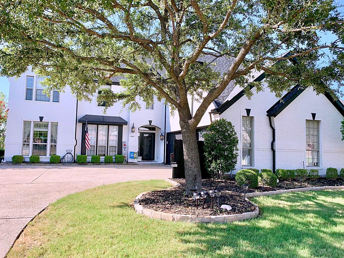 White brick home with a dark shingle roof behind a large live oak and a circular drive